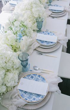 the table is set with blue and white plates, silverware, and hydrangeas