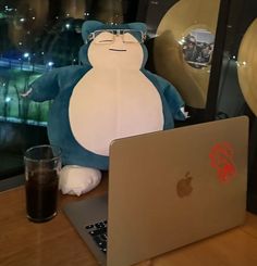 a stuffed animal sitting on top of a laptop computer next to a glass filled with liquid