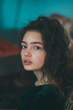 a woman with curly hair sitting on a couch looking off to the side while staring into the distance