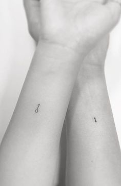 two small tattoos on the wrist that are both black and white, one with an arrow