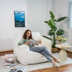 a woman is sitting on a bean bag chair reading a magazine in her living room