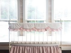 a white crib with pink ruffles in front of two windows