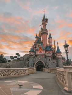 the entrance to disneyland's castle is lit up at sunset with clouds in the background