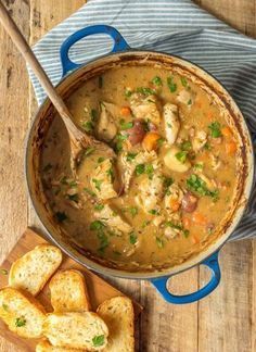 a blue pot filled with chicken and vegetable soup next to some slices of bread on a cutting board