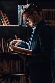 a man standing in front of a bookshelf holding a book and looking at it