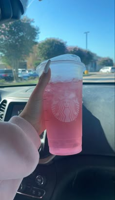 a person holding up a pink drink in their car