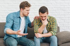 two men are sitting on a couch and one is holding his hand to his face