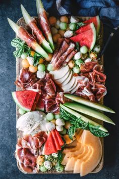 an assortment of meats and vegetables on a platter with cheese, tomatoes, watermelon, cucumber, lettuce