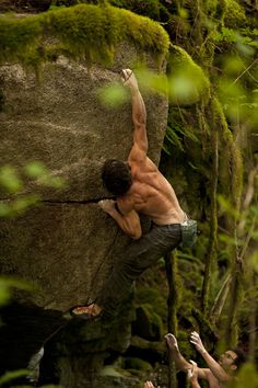 a man climbing up the side of a rock with his hands in the air while others look on