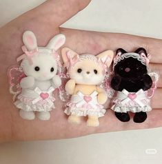 three small stuffed animals are sitting on someone's hand, one is wearing a pink and white dress