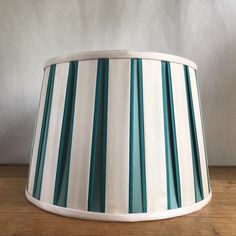 a green and white striped lamp shade on a wooden table with grey wall in the background