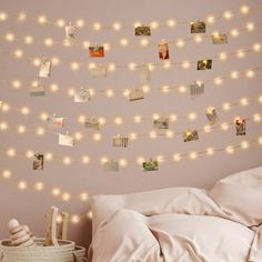 a bed with white sheets and string lights hanging from the wall above it, next to a wicker basket