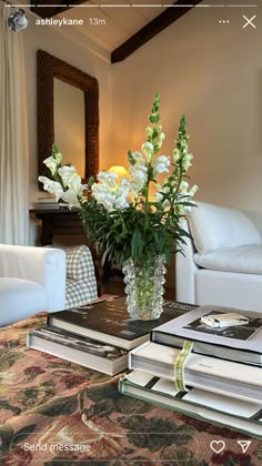 flowers in a vase sitting on top of two books next to a couch and chair