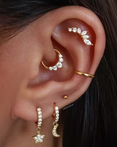 a woman wearing three different types of ear piercings with stars and moon designs on them