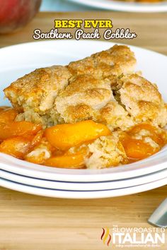 a white plate topped with peach cobbler on top of a wooden table next to sliced peaches