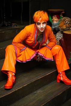 a man with painted face and orange pants sitting on some steps next to a leopard