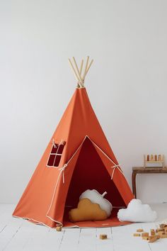 an orange teepee tent sitting on top of a white floor next to a wooden table