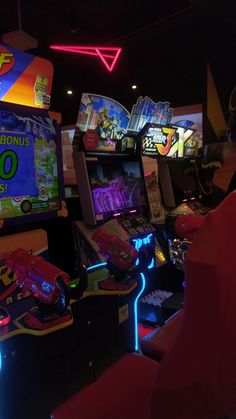 two people playing video games in a dark room with neon lights on the ceiling and arcade machines behind them