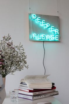 a neon sign that reads deep river please on it next to books and a vase with flowers