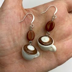 a pair of earrings with coffee and cream on them in the palm of someone's hand