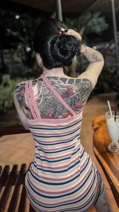 a woman sitting at a table with her back to the camera and tattoos on her body