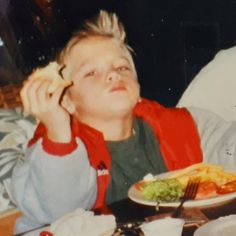 a young boy sitting at a table with food in front of him and looking up to the sky