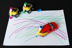 two toy cars are on top of a paper with colored crayons and markers