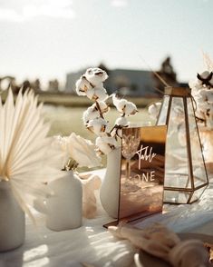 a table topped with white flowers and vases filled with cotton floss next to an open book