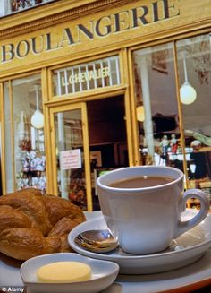 there is a cup of coffee and croissants on the table in front of this shop