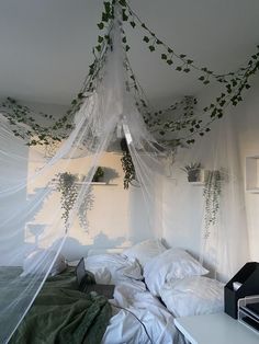 an unmade bed with white sheets and green plants hanging from the ceiling