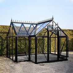 a small black glass house sitting in the middle of a gravel area next to a hedge