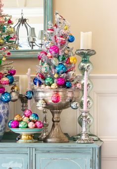 a christmas tree is decorated with ornaments and candles on a blue dresser in front of a mirror