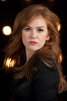 a woman with long red hair is posing for a photo in front of some lights