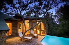 a wooden deck next to a swimming pool with chairs around it and trees in the background