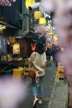 a woman walking down a street next to lots of boxes and lights hanging from the ceiling