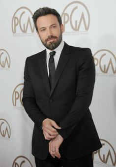 a man in a suit and tie standing on a red carpet with his arms crossed