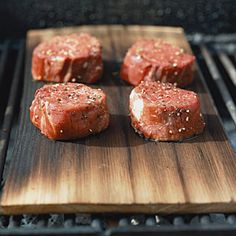 four pieces of raw meat on a wooden cutting board next to an open bbq