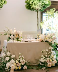 a table with white flowers and candles on it in front of two trees that have green leaves