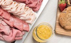 an assortment of meats and cheeses on a cutting board with a jar of mustard