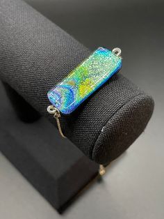 a blue and green pendant sitting on top of a black piece of cloth next to a wooden stand