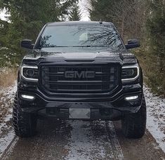 the front end of a black truck on a snowy road with trees in the background