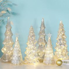 lighted glass christmas trees are displayed on a table