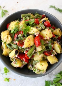 a bowl filled with potato salad on top of a white table next to cilantro and parsley