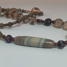 What an unusual combination of subtle colors and textures - starting off with the stunning off centered antique banded agate (it even has an eye to the beautifully faceted smoky quartz beads, to the various bronze tone beads, sterling spacers/box clasp and rich, rich burgundy garnets (raw tumbled and finished).  Perfect colors for this fall's fashion trends.  All over the world since ancient times, mankind has feared the 'evil eye' and used talismans or stone/glass beads to protect themselves. Elegant Jasper Gemstone Jewelry, Elegant Handmade Gemstones For Healing, Elegant Handmade Healing Gemstones, Elegant Hand-strung Agate Necklace, Vintage Gemstone Beads Jewelry For Meditation, Handmade Spiritual Necklace For Layering, Elegant Beaded Chalcedony Jewelry, Elegant Brown Jewelry For Meditation, Elegant Handmade Jasper Necklaces