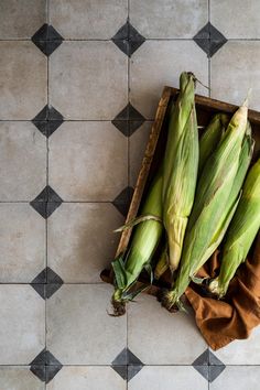 corn on the cob in a wooden box sitting on a tile floor next to a brown cloth