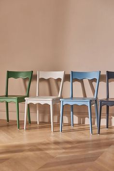 four chairs lined up against a wall in different colors and sizes, one is blue, the other is green