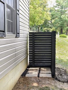 a black gate sitting next to a house on top of a grass covered field near a tree