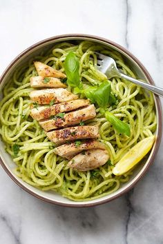 a bowl filled with pasta and chicken on top of a marble table next to a fork