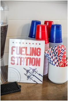 a wooden table topped with red, white and blue paper cups next to a sign