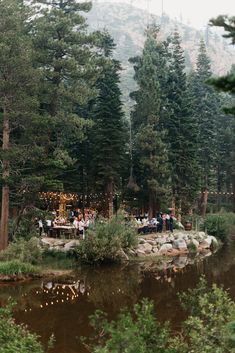 a group of people sitting at a picnic table next to a river in the woods